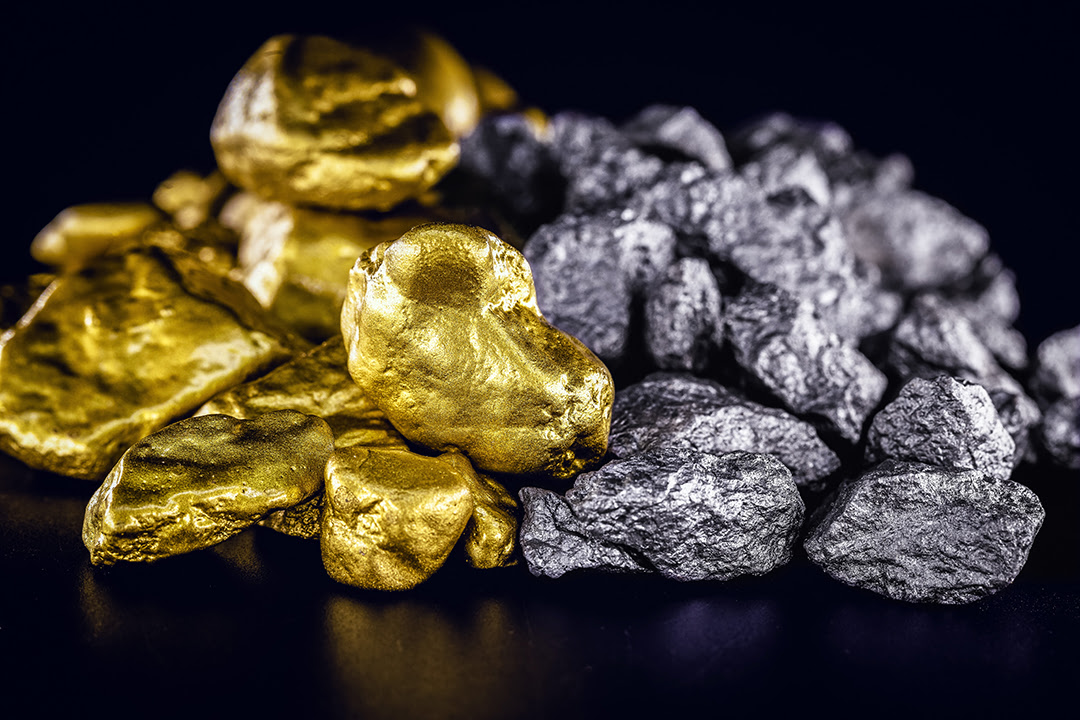 Nuggets of gold and silver rest in a pile on a black background.