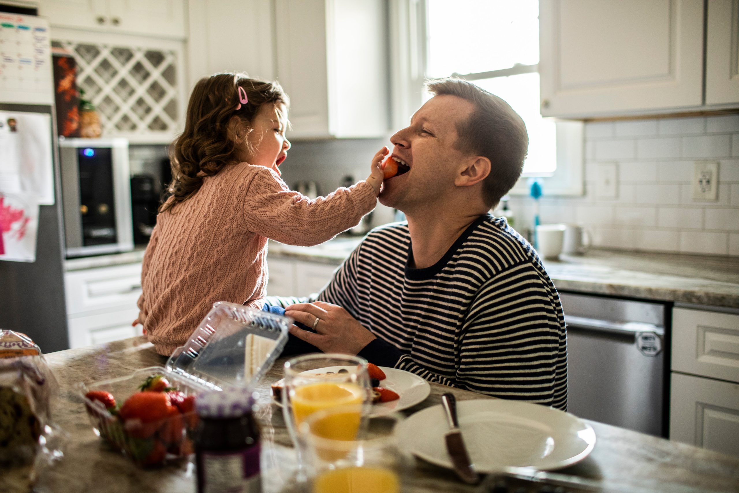 young girl feeding her dad a strawberry