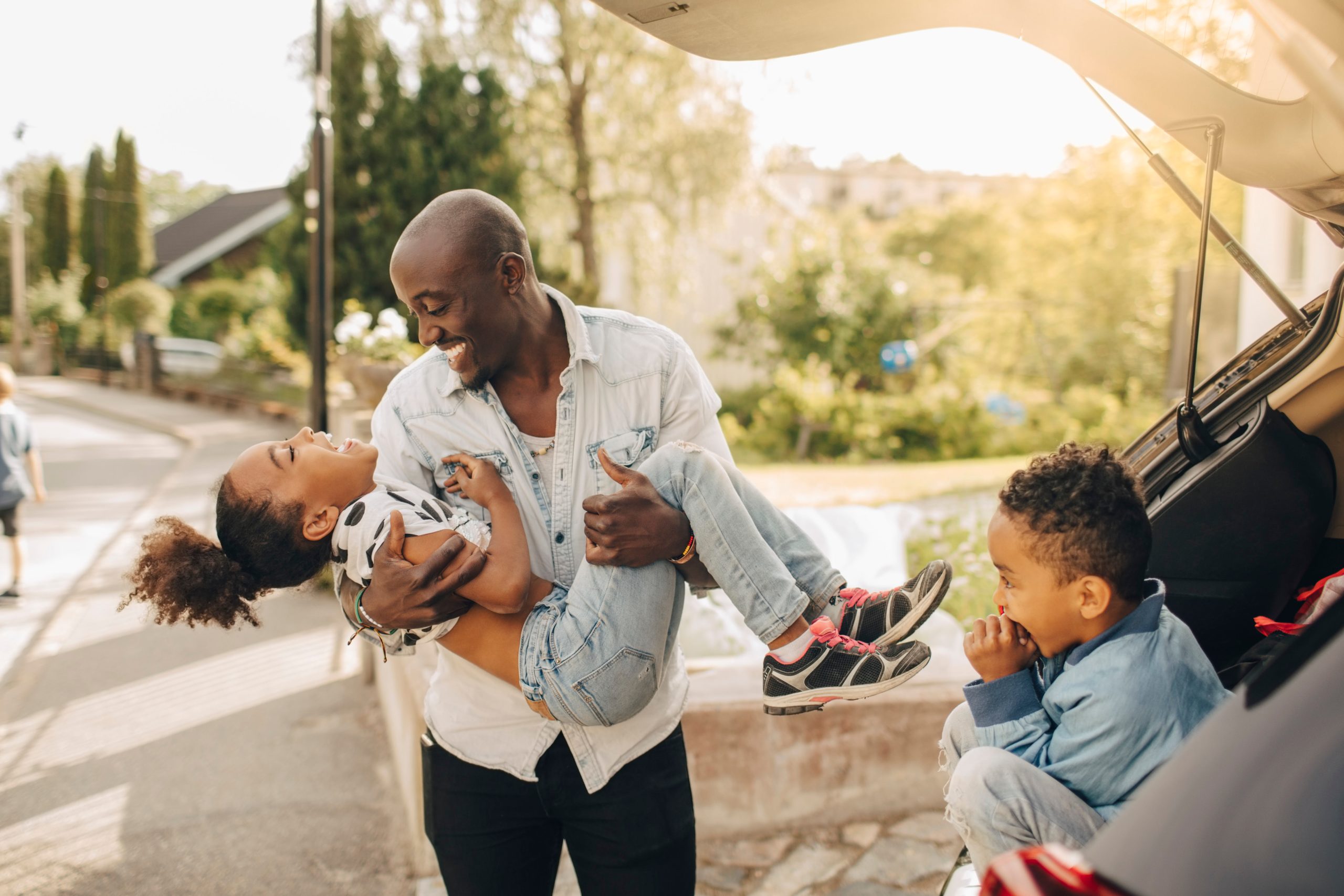 dad and two kids playing outside of car